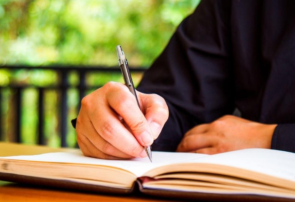It's a guy write a notebook in the patio with a black t-shirt and in the back is a fun an tree.